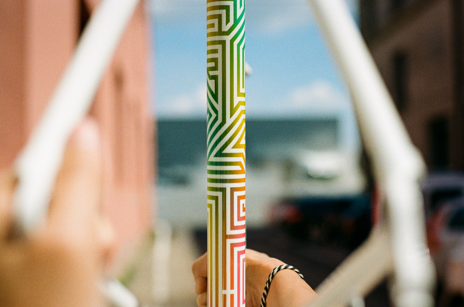 A custom seatpost finished in a rainbow geometric pattern, held up against a sunlit street